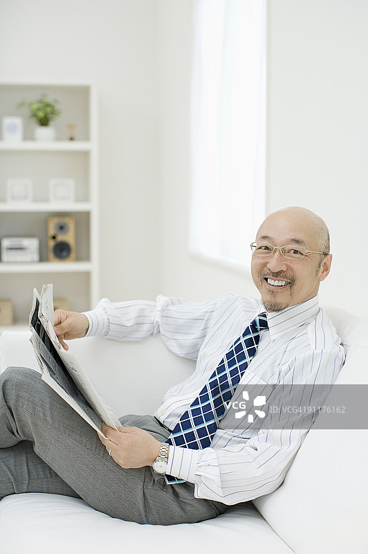 中年男人坐在沙发上，读报纸图片素材