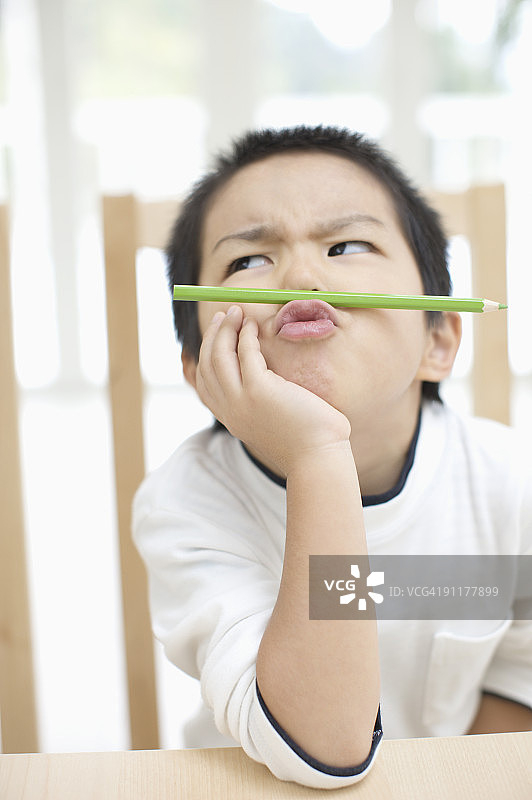 男孩用鼻子和嘴唇夹着铅笔图片素材