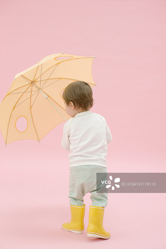 穿橡胶靴 holding 雨伞的男孩，影棚拍摄，后视图图片素材