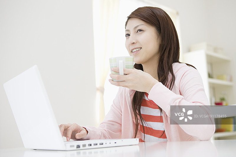 手持马克杯使用笔记本电脑的年轻女人图片素材