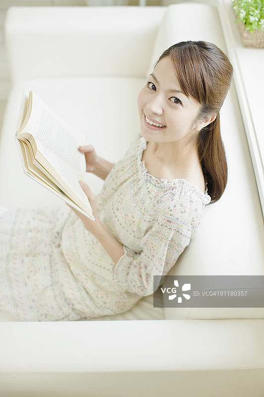 女人坐在沙发上看书，高角度视角图片素材