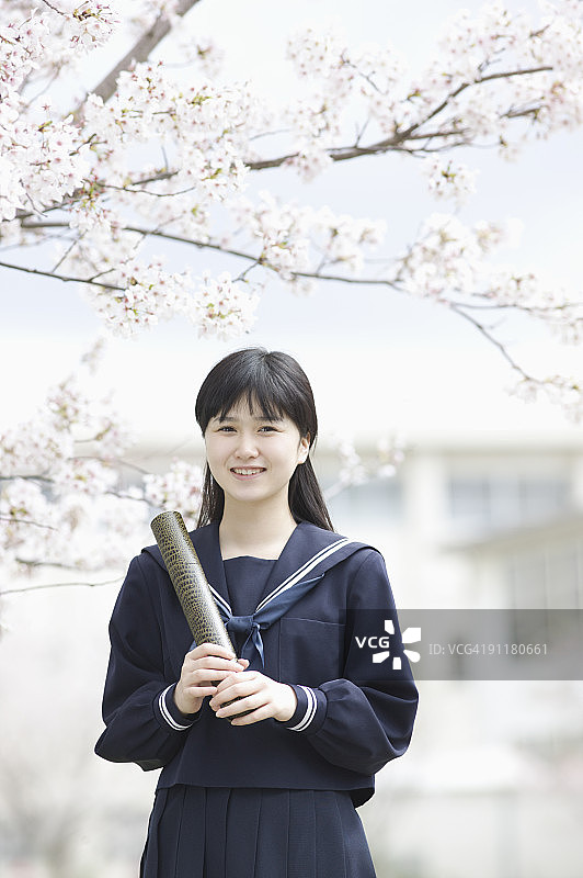 穿着校服，拿着毕业证书在樱桃树旁的微笑少女图片素材