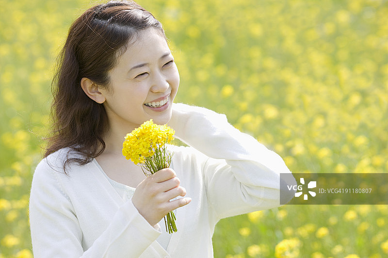 手捧鲜花站在油菜花田里的年轻女人图片素材