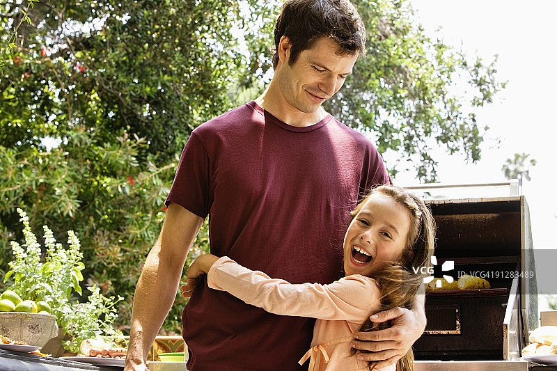 女孩在烧烤架前拥抱父亲图片素材