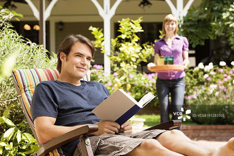 男人在读书，女人端着饮料走近图片素材