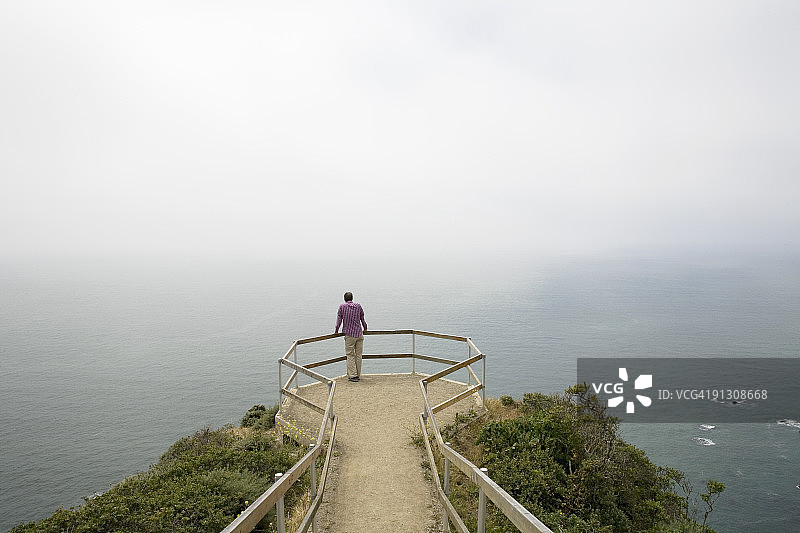 男子站在悬崖上，眺望雾中的大海图片素材