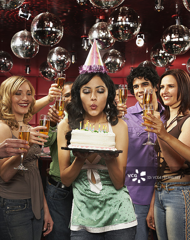 戴着派对帽的女人吹灭生日蛋糕上的蜡烛图片素材