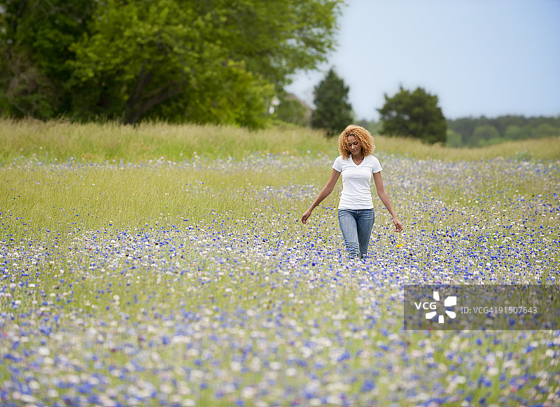 年轻女人穿过鲜花盛开的田野图片素材