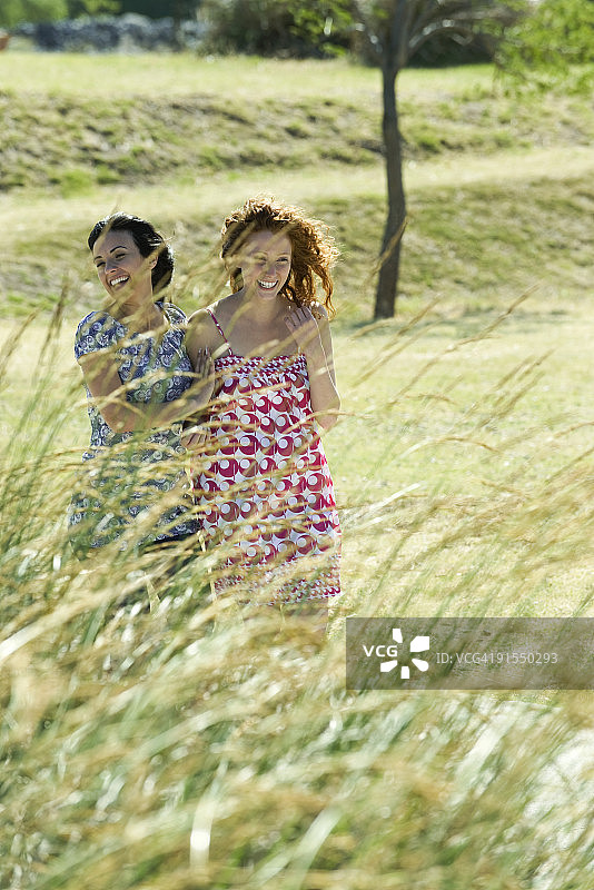 在户外一起欢笑的两位年轻女子，前景是茂盛的草地图片素材