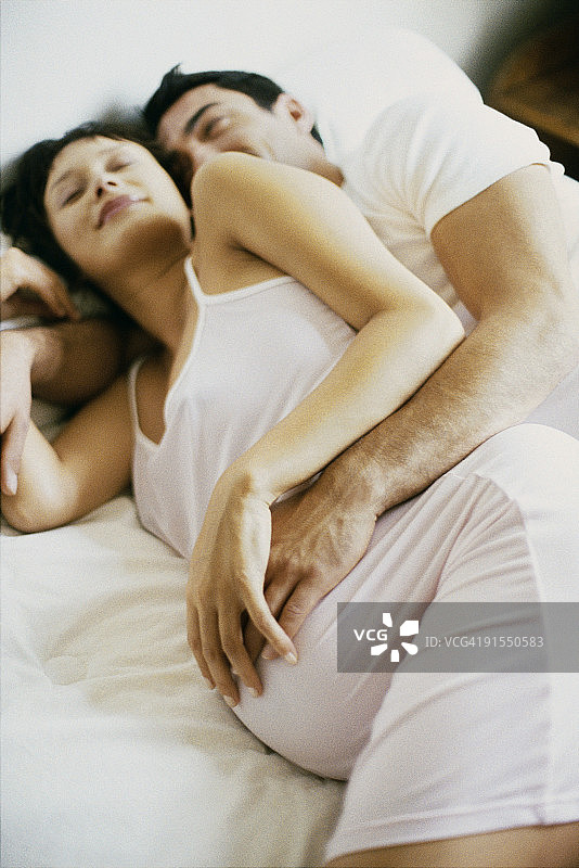 情侣一起躺在床上，都抚摸着孕妇的肚子图片素材