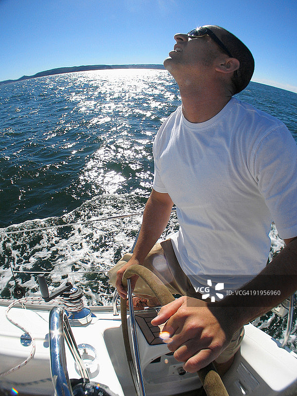 一名船长在碧水湾巡航时，在游艇上掌舵图片素材