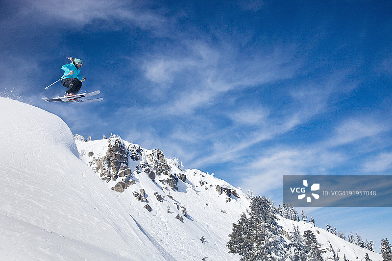 女滑雪者跃入新雪，背景是山脉蓝天图片素材