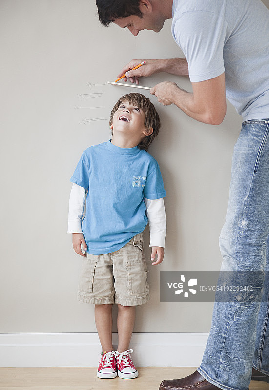 父亲在墙边给儿子量身高图片素材