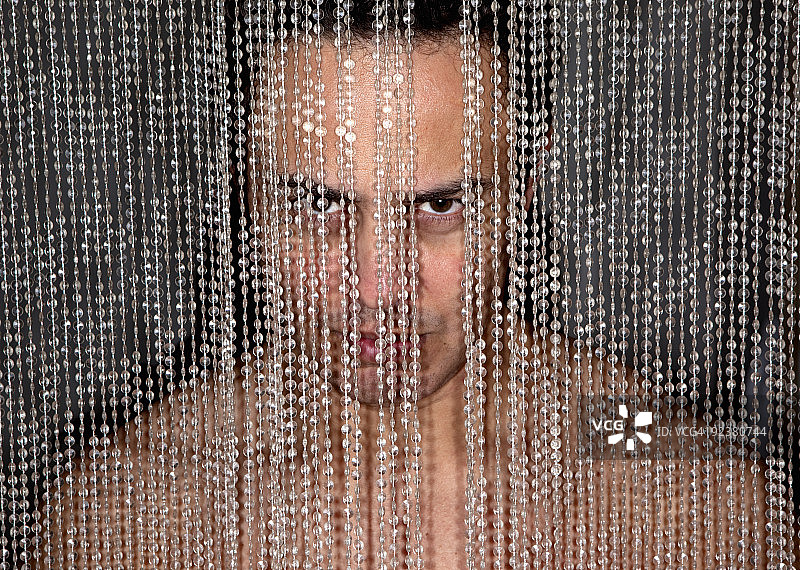 一个44岁的男人躲在一堵串珠墙后面。图片素材