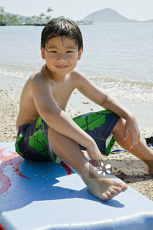 微笑的男孩坐在沙滩上的冲浪板上图片素材