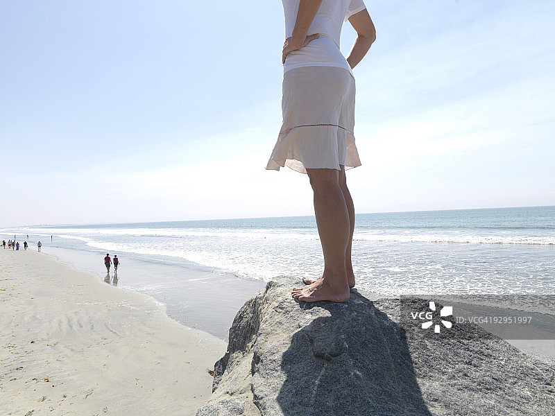 女人站在岩石岬角上，俯瞰海滩图片素材