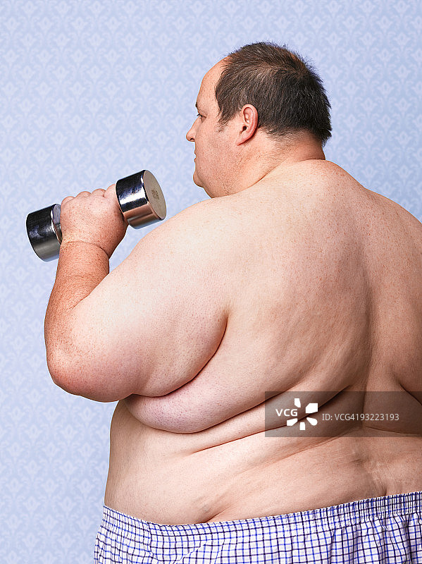 从背后看超重男子用哑铃锻炼图片素材