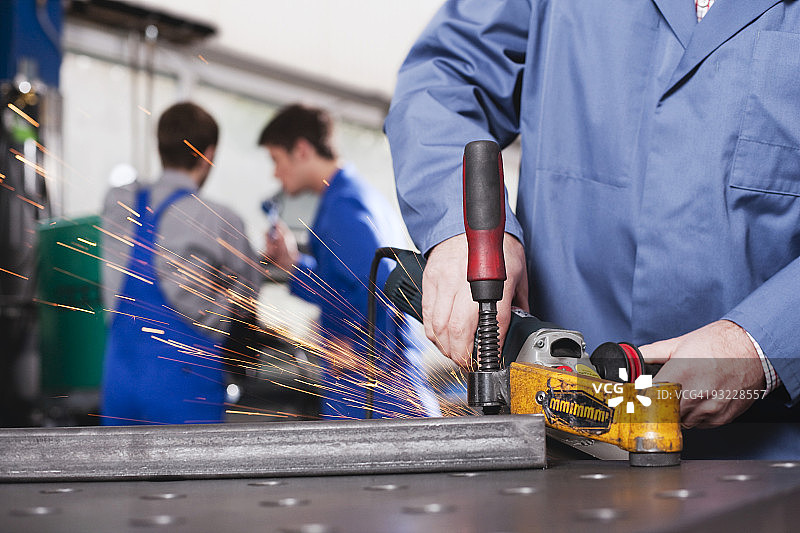德国诺伊基尔：使用砂轮的人，背景是学徒和工头图片素材