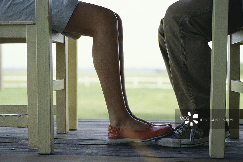 年轻夫妇在桌旁相对而坐，女子双脚接触男子，低角度拍摄图片素材