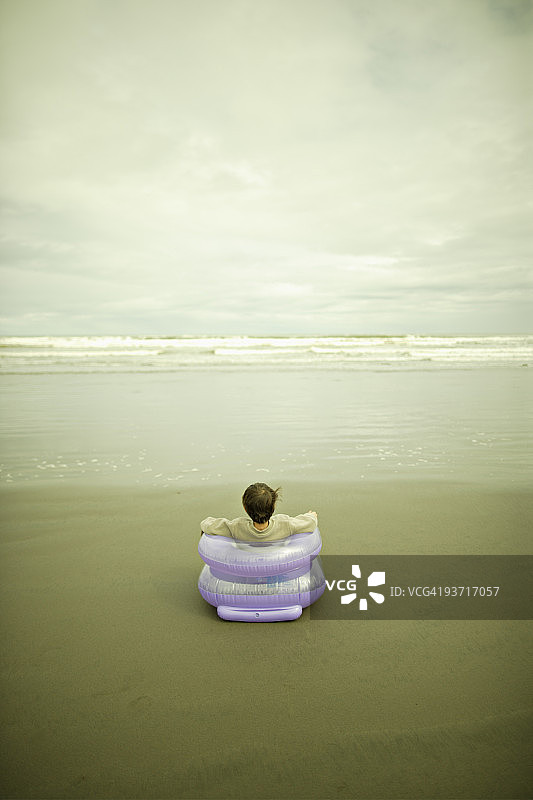 男孩坐在沙滩的充气椅上图片素材