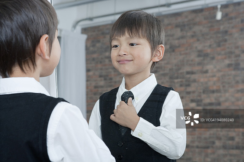 男孩在镜子前整理领带，面带微笑图片素材