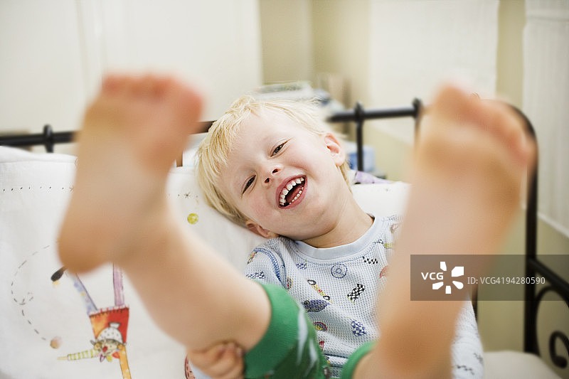 抬起脚躺在床上的幼儿男孩图片素材