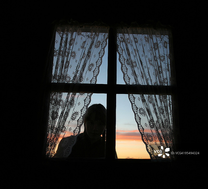 夕阳下在窗边窥视的年轻女孩图片素材