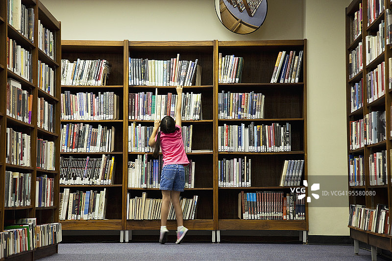 在图书馆书架旁读书的女孩图片素材
