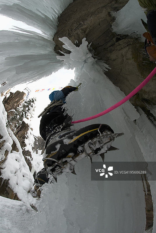 女子冰攀冰冻瀑布，靴子和冰爪特写图片素材