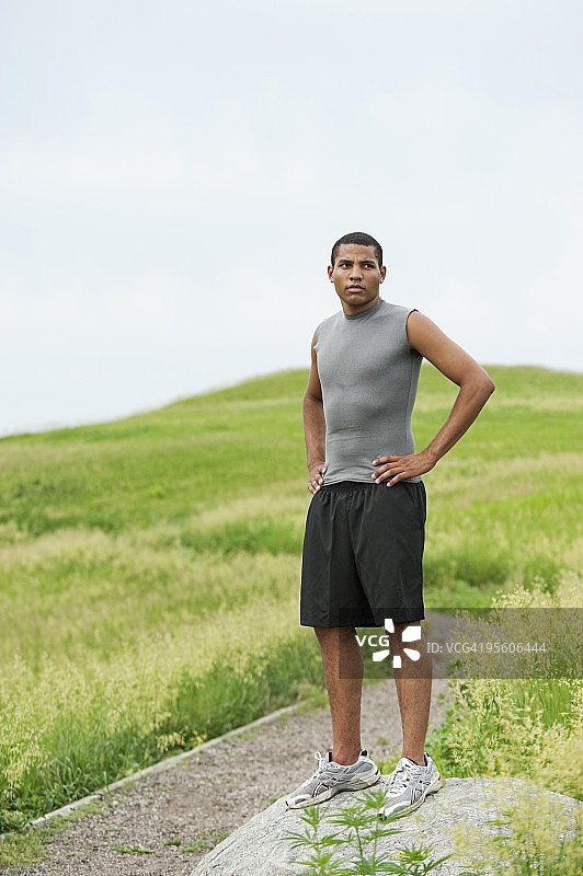 在绿色田野的砾石路上奔跑后，站在岩石上的青年男人图片素材