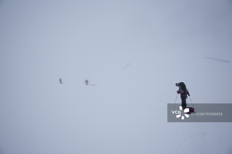 三名滑雪者在阿拉斯加德纳里国家公园的雾中冰川上徒步旅行图片素材