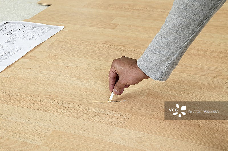 男子将复合材料涂抹在木地板上的划痕上图片素材