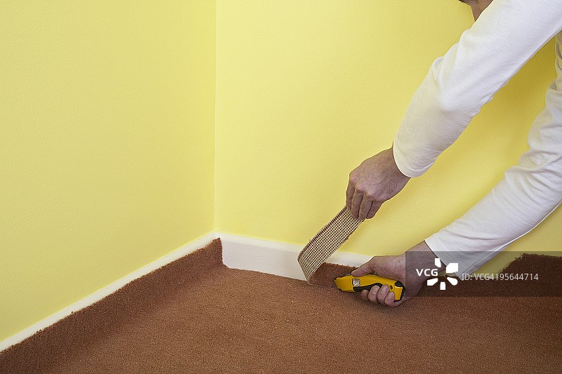 男人使用美工刀切割地毯，靠着踢脚板的边缘图片素材