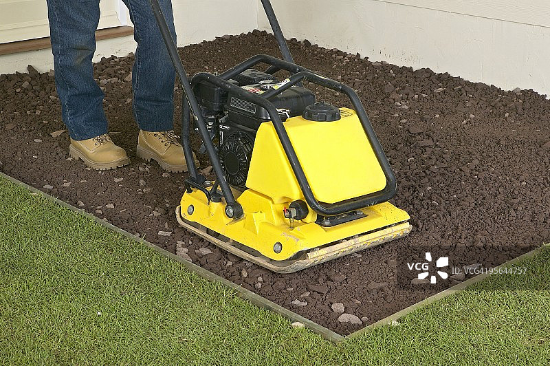 男人在草地旁用平板夯压机压实硬质材料，特写图片素材