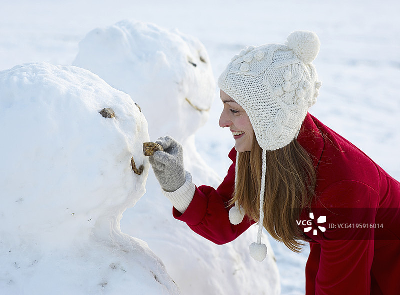 年轻女人给雪人装上鼻子图片素材