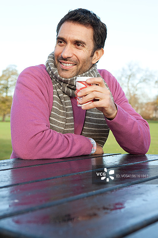 男子坐在公园的桌子旁，手持热饮图片素材