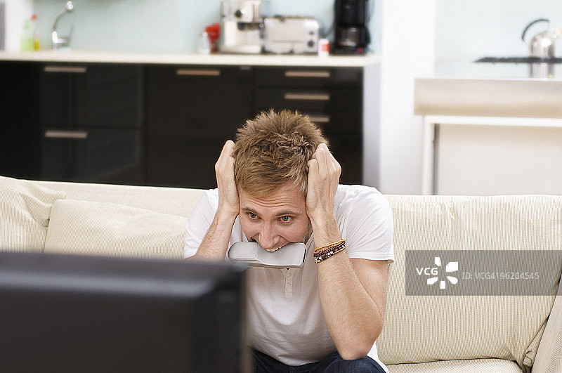 紧张的男人咬着电视遥控器，拽着头发图片素材