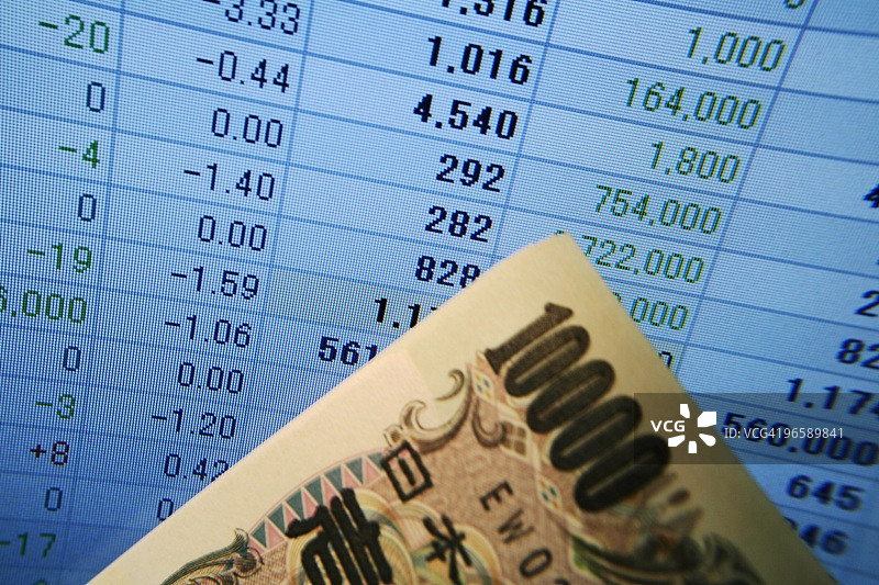电脑屏幕前的10日元和100日元纸币，屏幕上显示财务报表图片素材