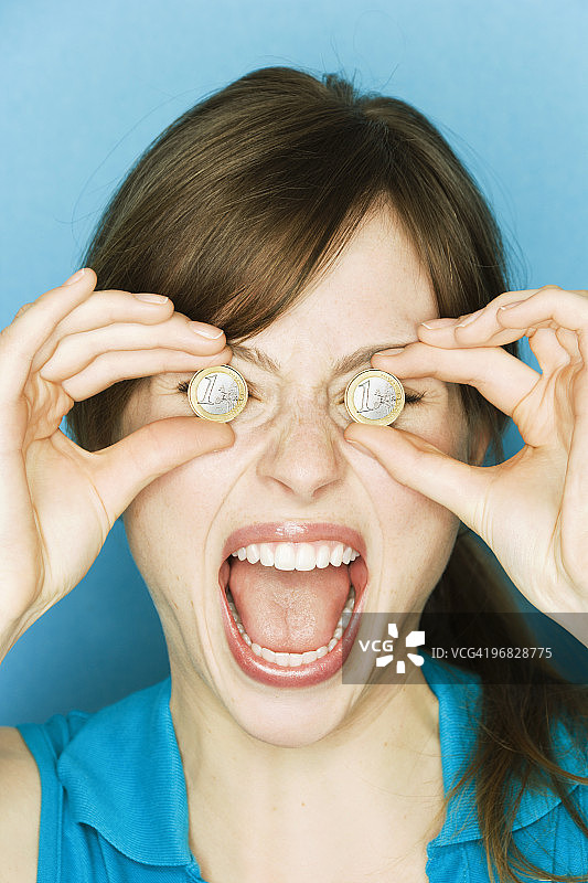 年轻女人举起欧元硬币遮住眼睛图片素材