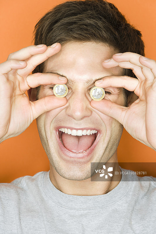 手持欧元硬币遮住眼睛的年轻男人图片素材