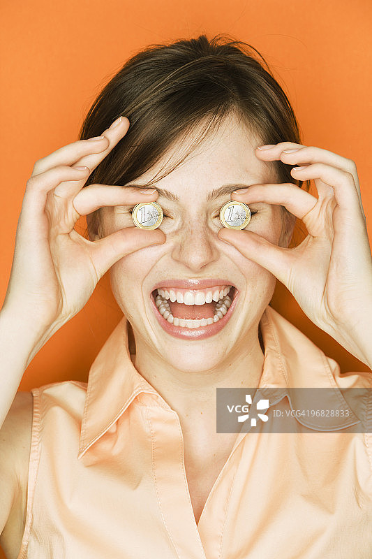 年轻女人举起欧元硬币遮住眼睛图片素材