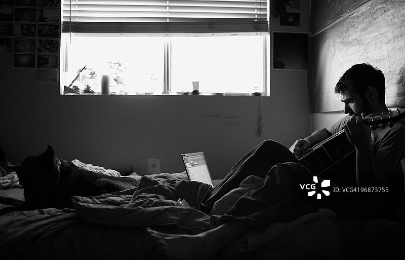 男人在床上弹吉他，狗狗相伴图片素材