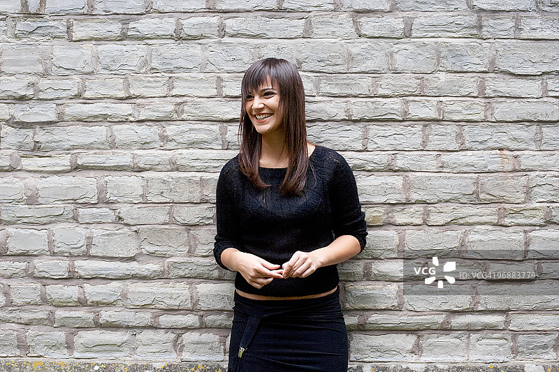 年轻女人微笑倚墙而立图片素材