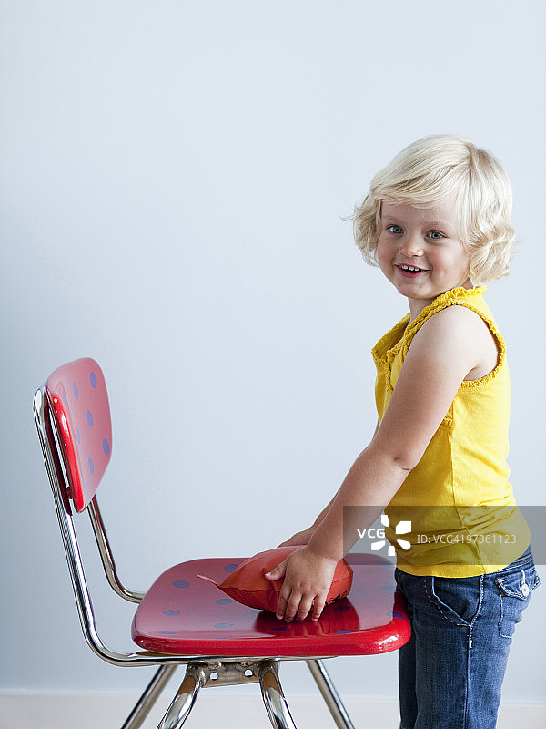 笑着把放屁垫放在椅子上的女孩（2-3岁），影棚拍摄图片素材