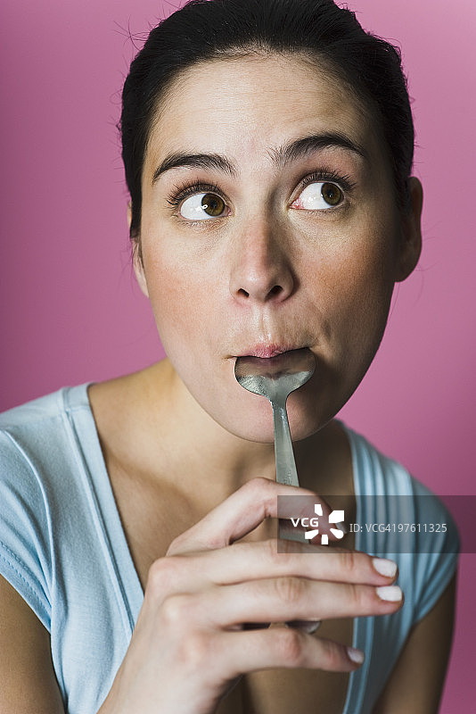 女人舔着勺子，看向别处图片素材
