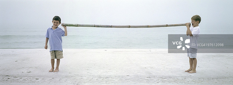 在海滩上通过竹竿互相交谈的两个男孩图片素材