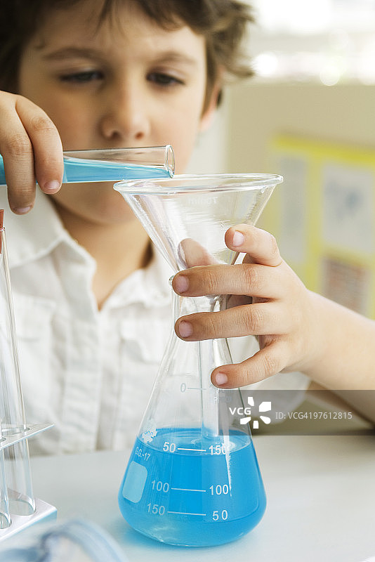男孩用漏斗将液体从试管转移到烧杯中图片素材