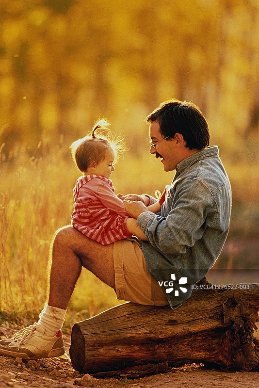父亲坐在原木上，和9-12个月大的女婴玩耍图片素材