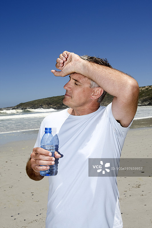 在海滩上手持一瓶水的年长男人图片素材