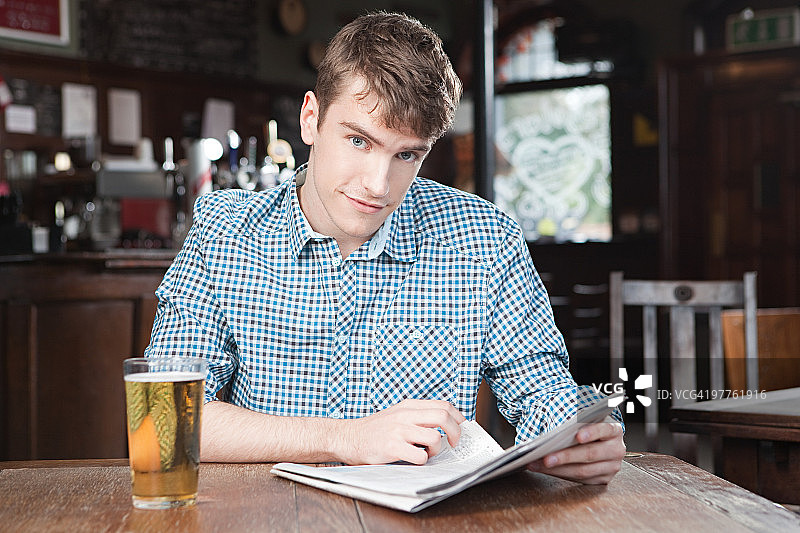 在酒吧看报纸喝啤酒的年轻人图片素材